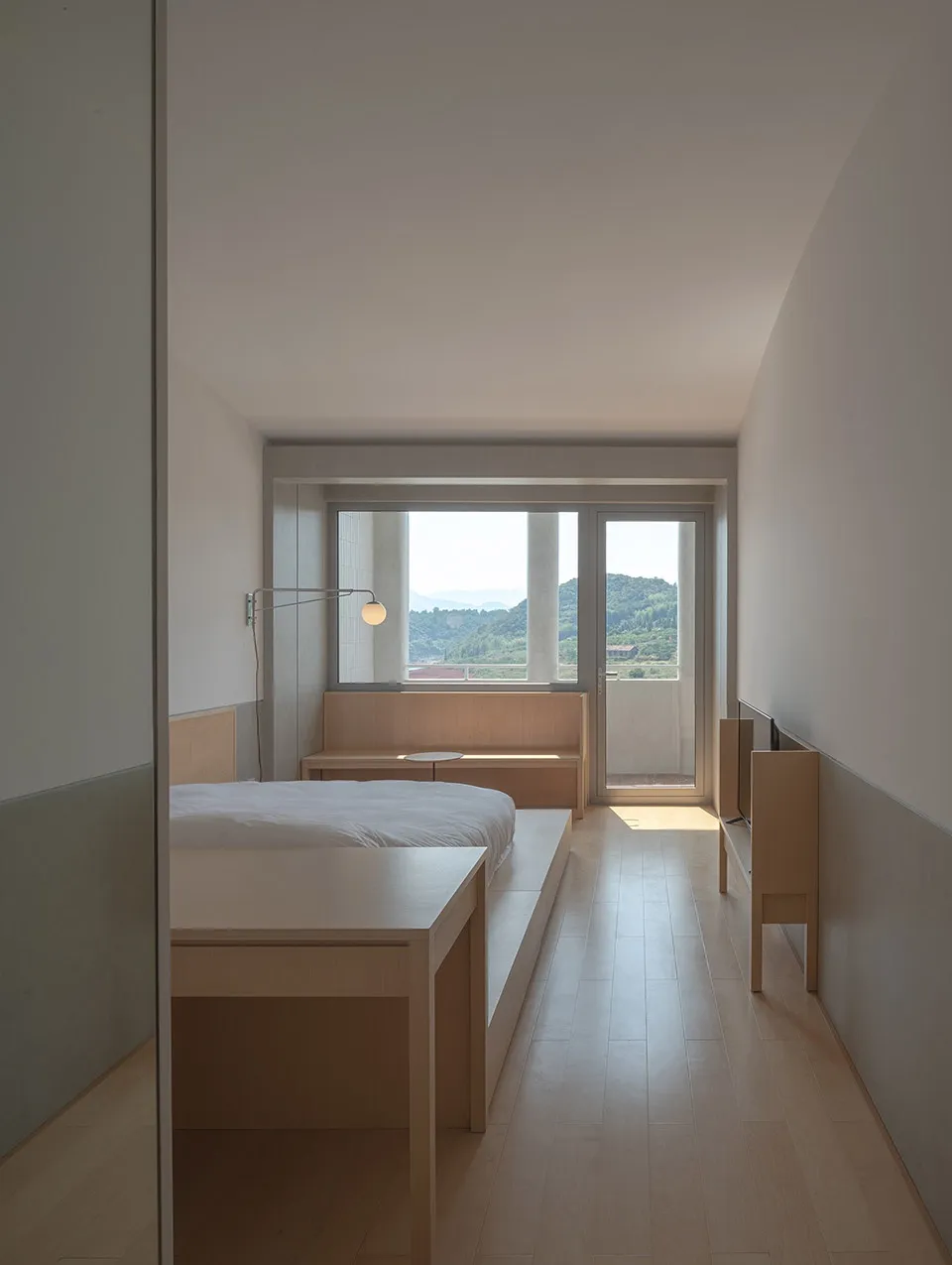 Modern bedroom featuring a wooden bed and bench with a view of the mountains through the large window.
