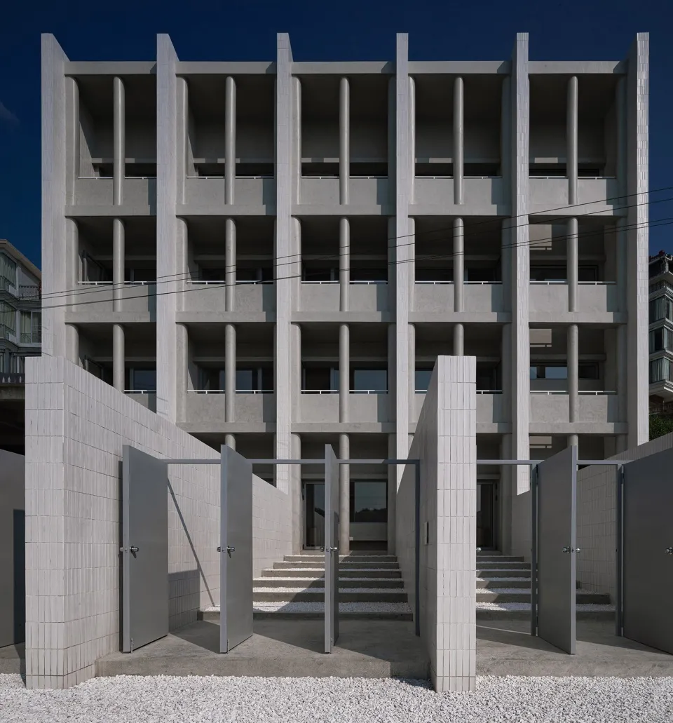 A modernist building with a concrete facade and vertical columns, featuring balconies and large windows.