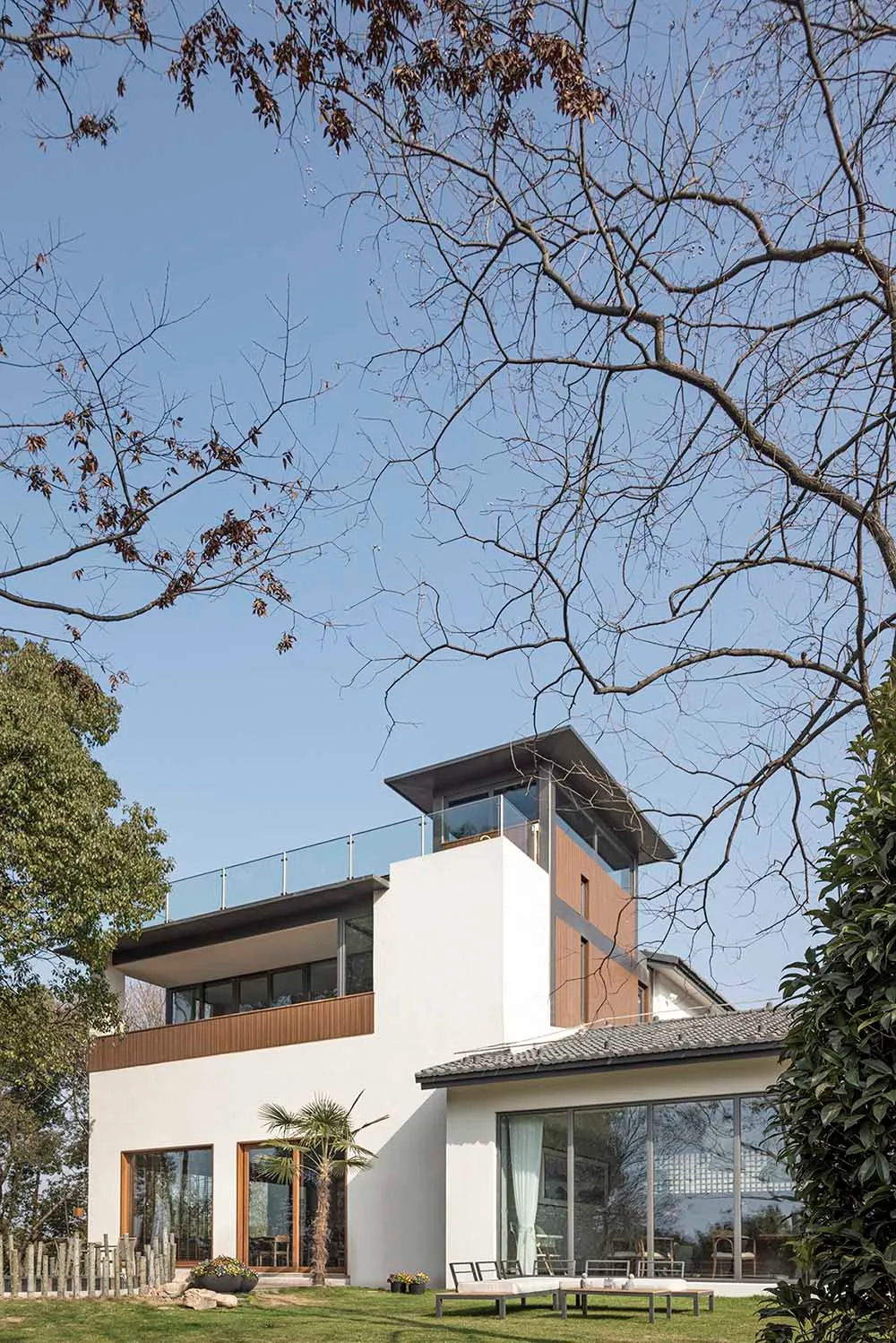 A modern house with white stucco exterior, featuring large glass windows and a rooftop deck.