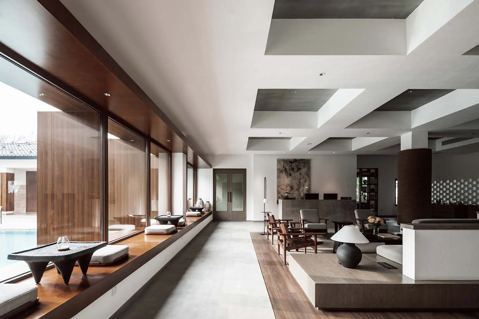 A modern living room with concrete walls and a large glass window overlooking a pool.