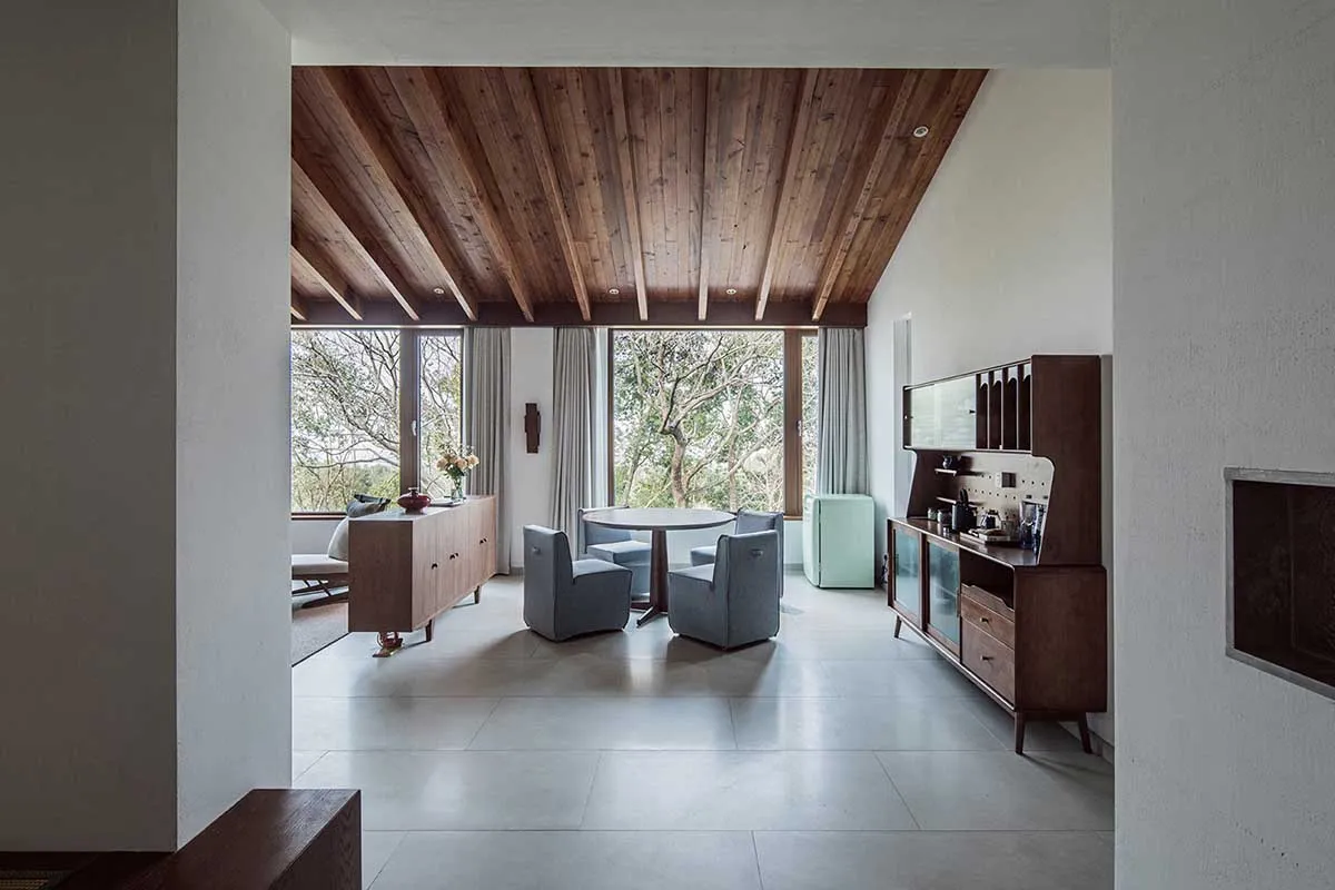 A modern living room with a wooden ceiling and floor, featuring a round table and blue chairs.