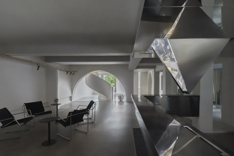 A modern lounge area with a concrete floor, metal chairs, and a glass-enclosed staircase.
