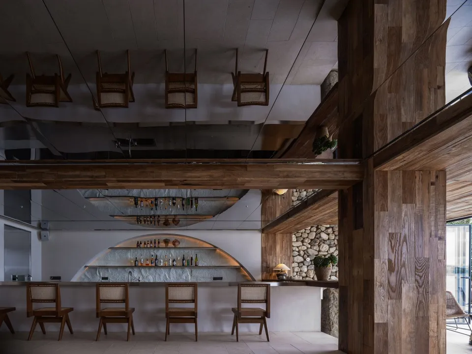 A modern restaurant bar with wooden chairs, a concrete countertop, and a rustic stone wall.