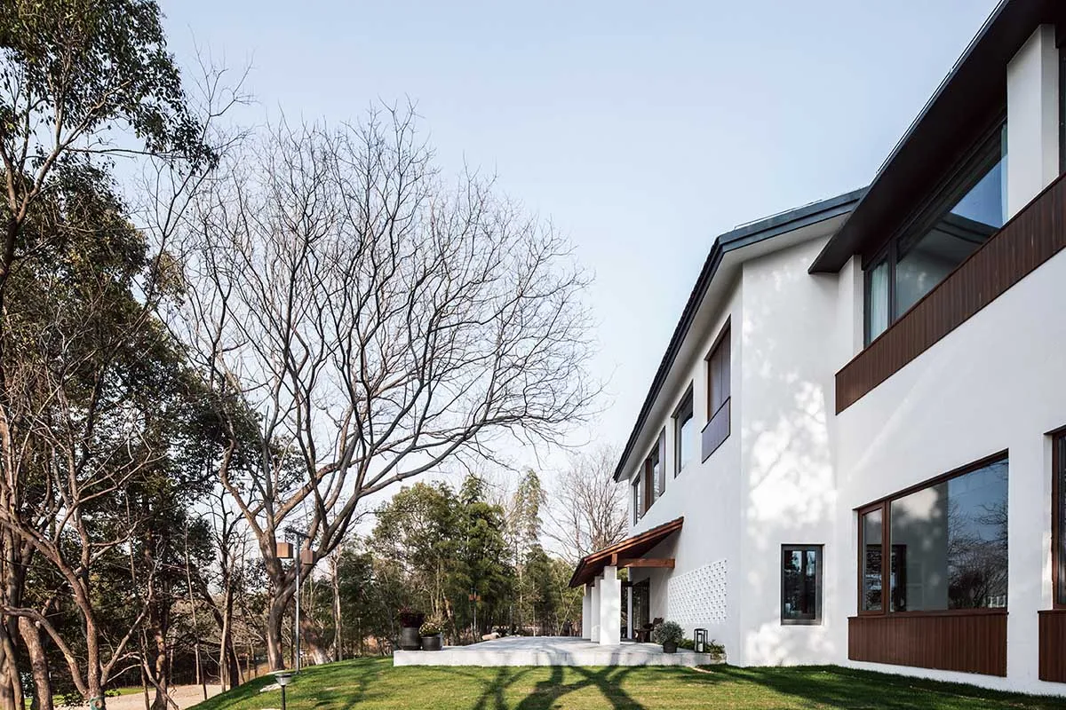 A modern residential home with a white exterior and concrete patio surrounded by trees.