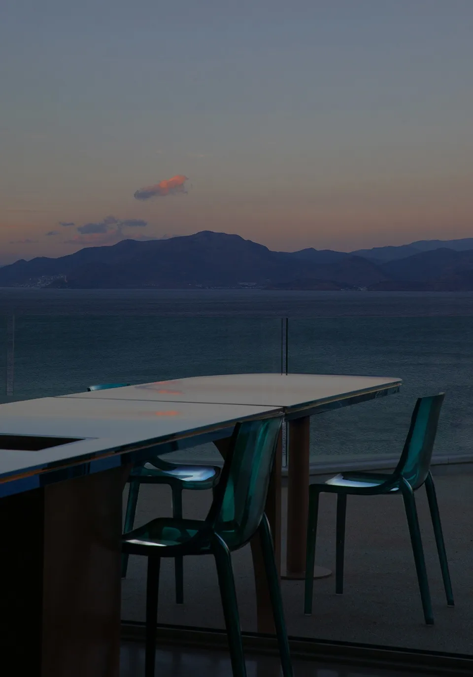 Glass dining table and chairs in a restaurant setting with a view of the sunset and mountains.