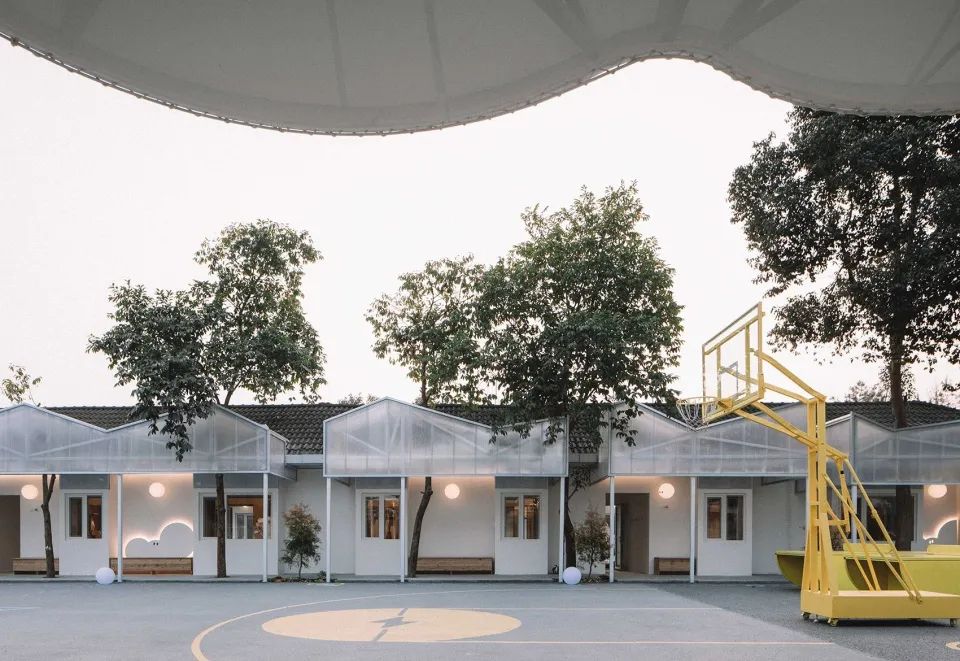 An outdoor basketball court with a glass-roofed pavilion and surrounding greenery on a clear day.