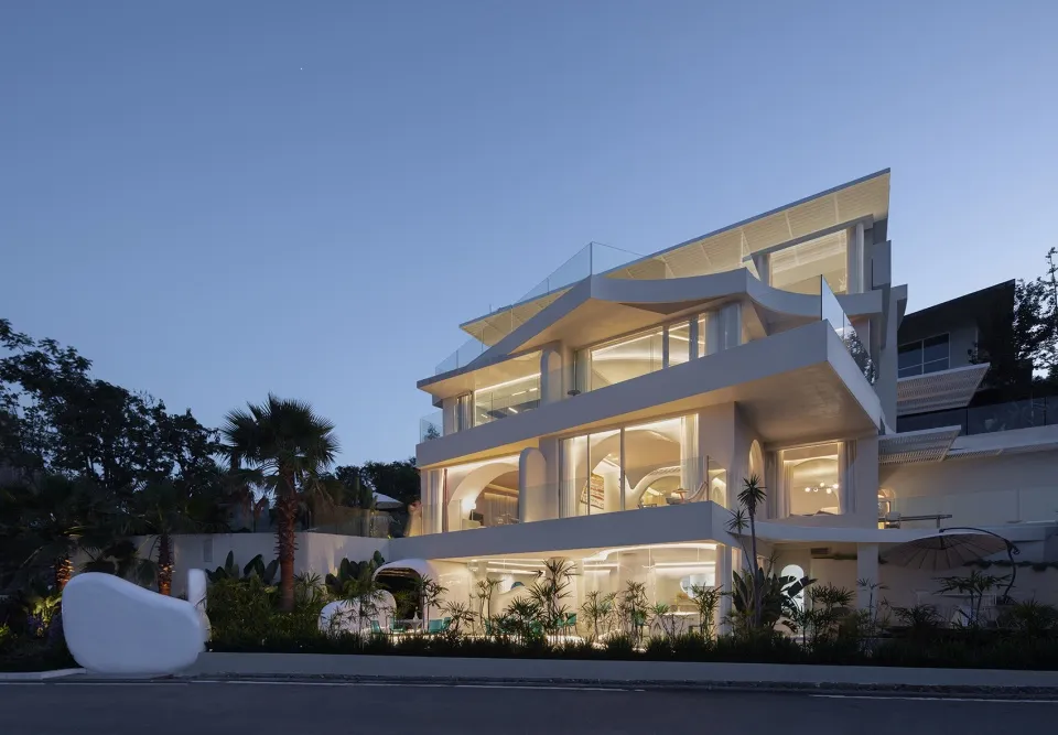 A modern house with a glass exterior, illuminated at dusk.