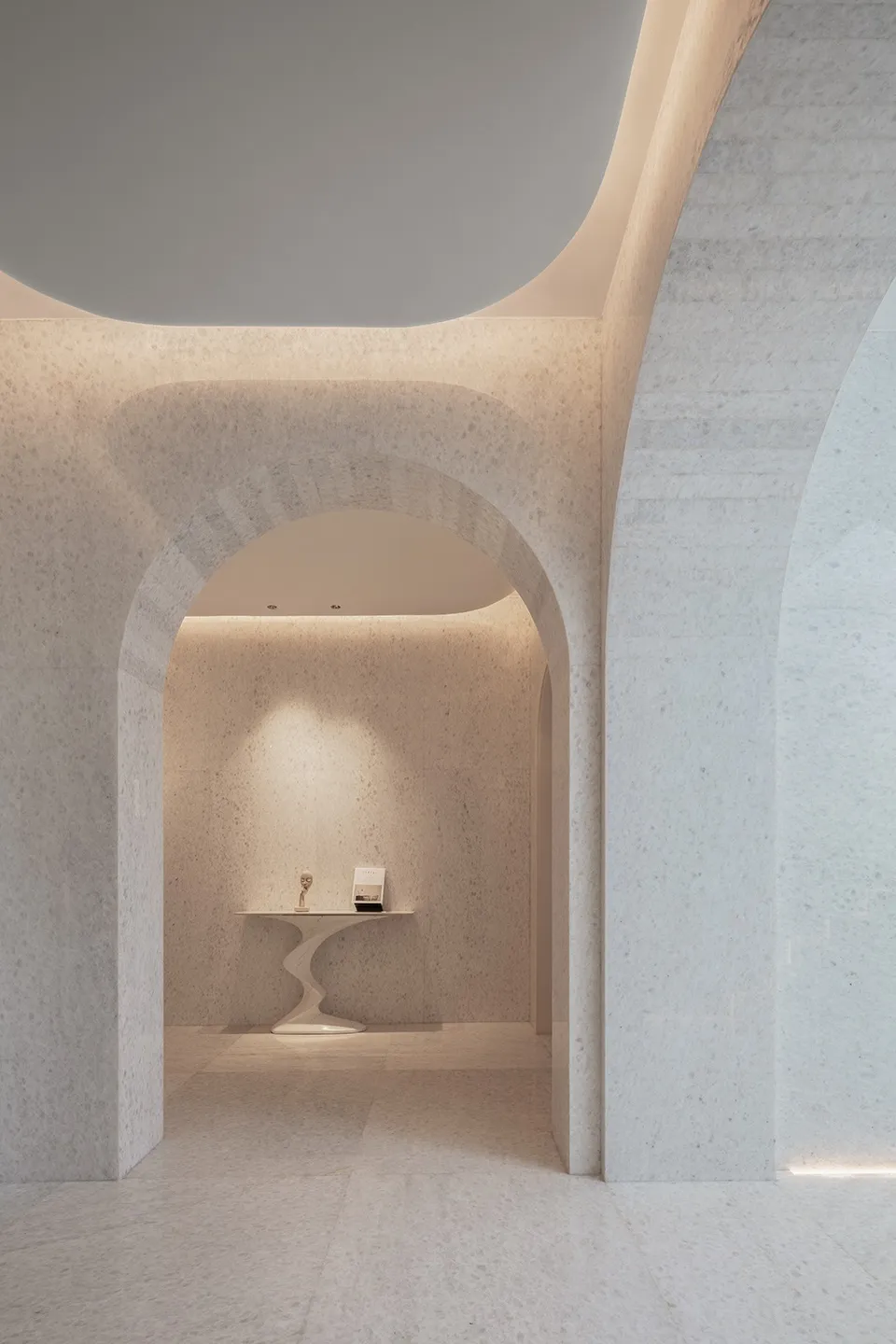 A minimalist marble lobby with arched doorways and curved table.