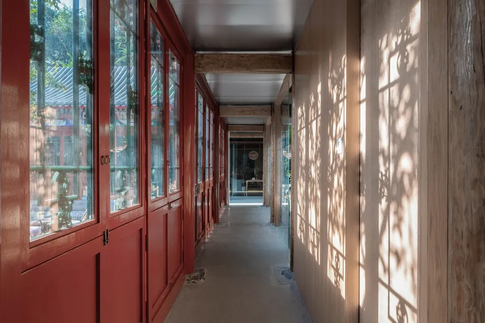 A corridor with red wooden doors and glass windows, scattered sunbeams, and wooden panels on the walls.