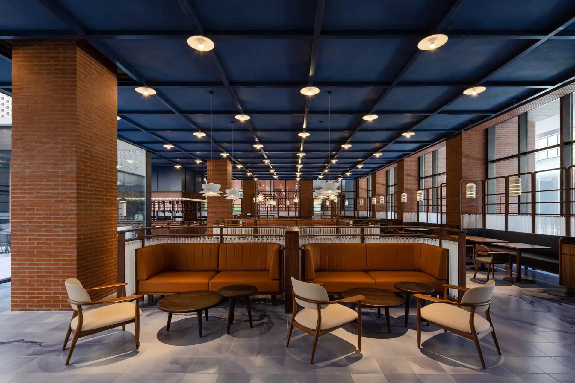 A spacious, industrial-themed restaurant interior with exposed brick walls, concrete pillars, and modern lighting fixtures.