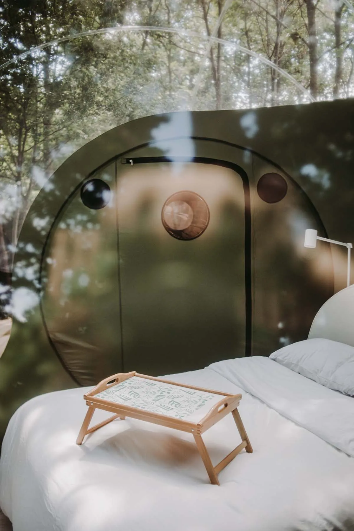 A minimalist bedroom with a white bed and wooden tray on top of it, set against a backdrop of a transparent dome structure vi