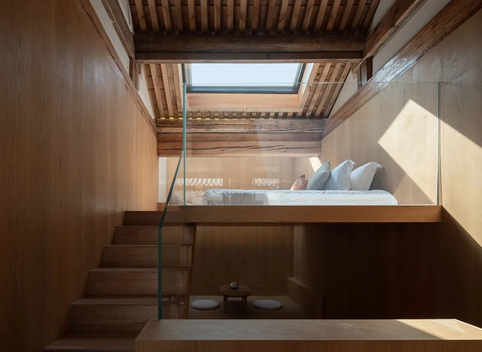 A modern bedroom featuring wooden elements, with a lofted bed and glass railing.