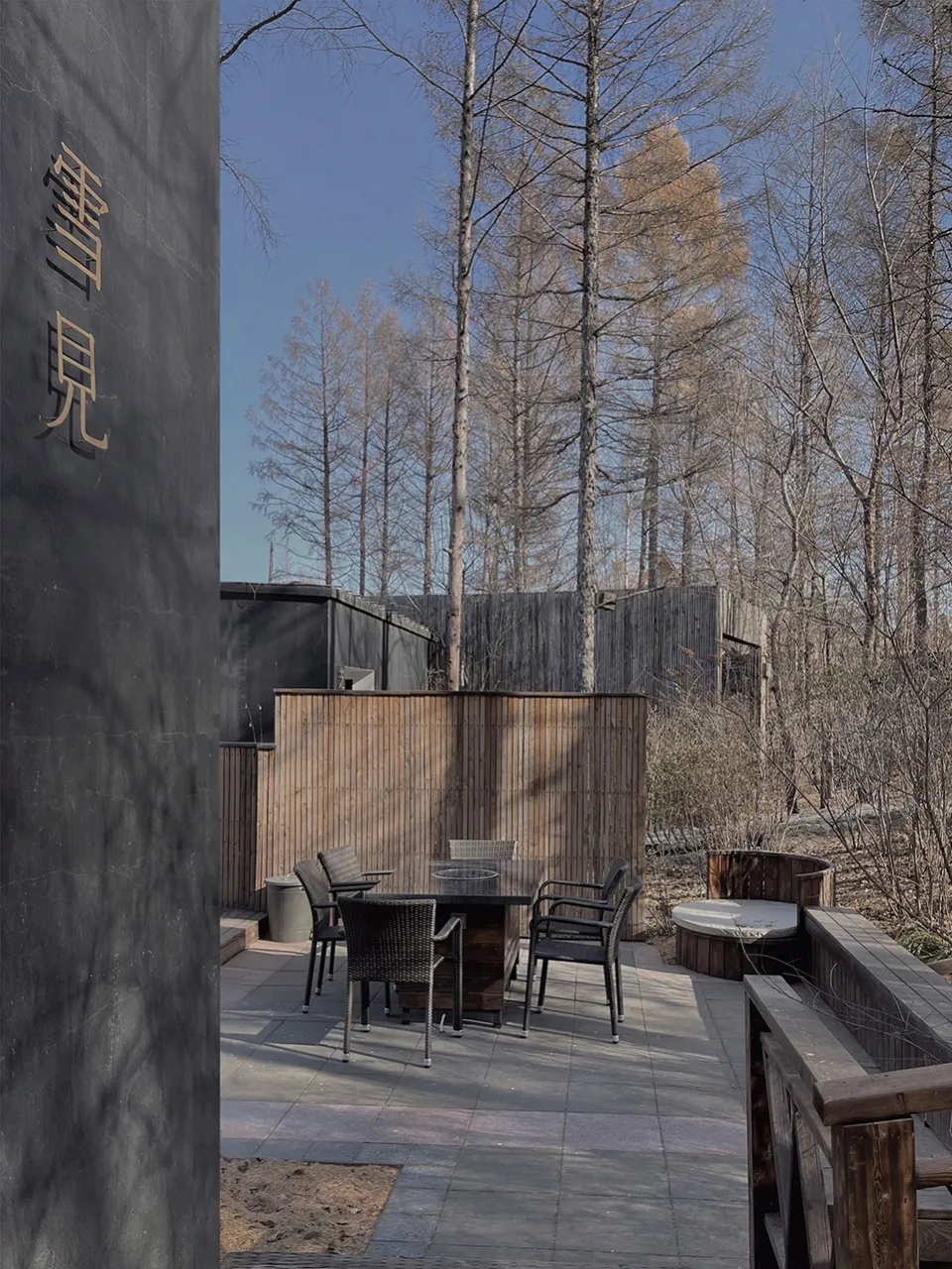 Modern outdoor patio area with wooden accents, glass panels, and stone flooring.
