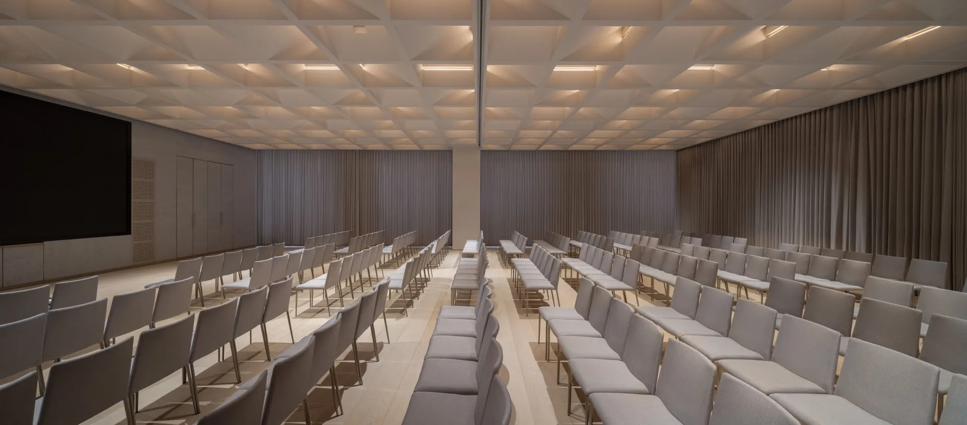 Multiple rows of fabric-covered chairs arranged in a spacious conference room with a minimalist design.