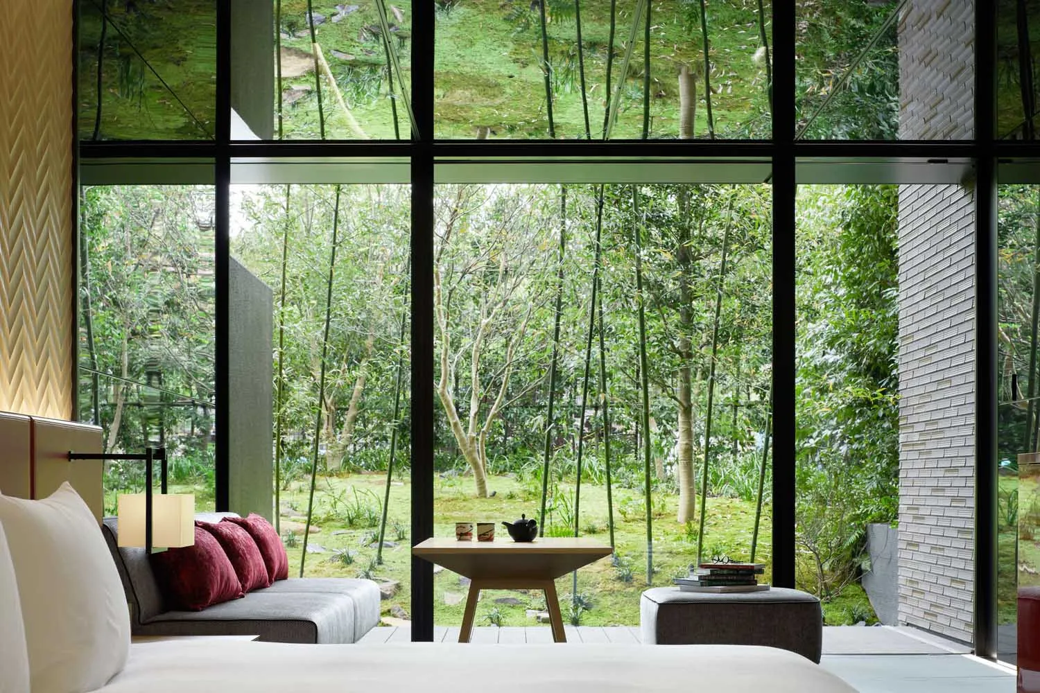 A modern bedroom featuring a glass wall overlooking a lush green garden.
