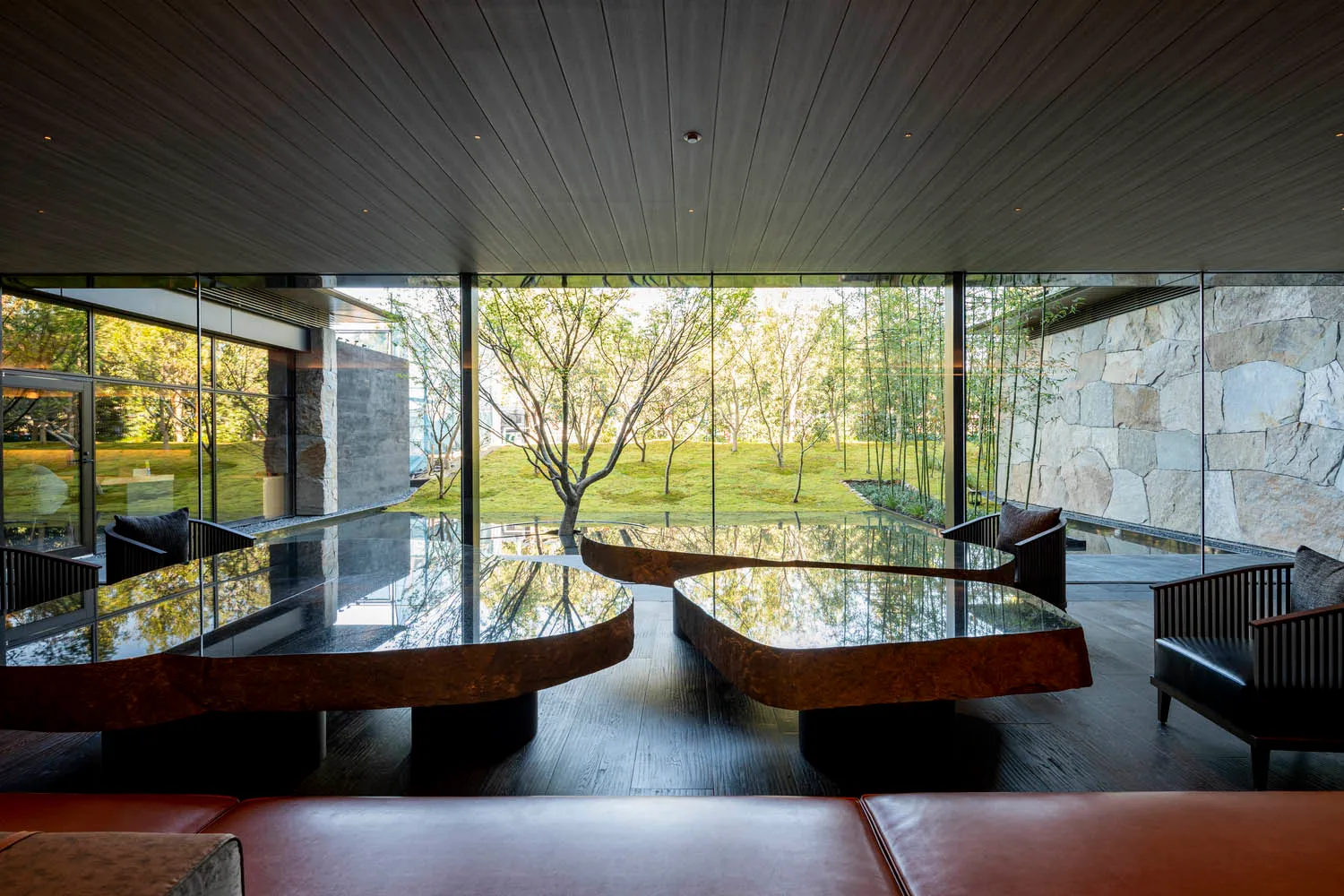 Modern interior design featuring a living room with wooden tables, glass walls, and leather seating.