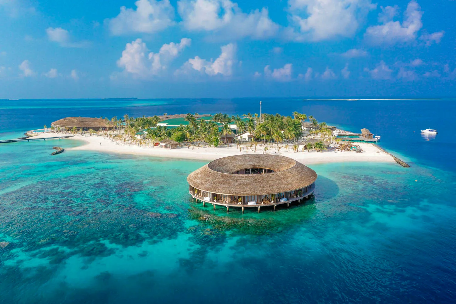 Aerial view of a resort island with a circular thatched-roof building and a white sandy shore.