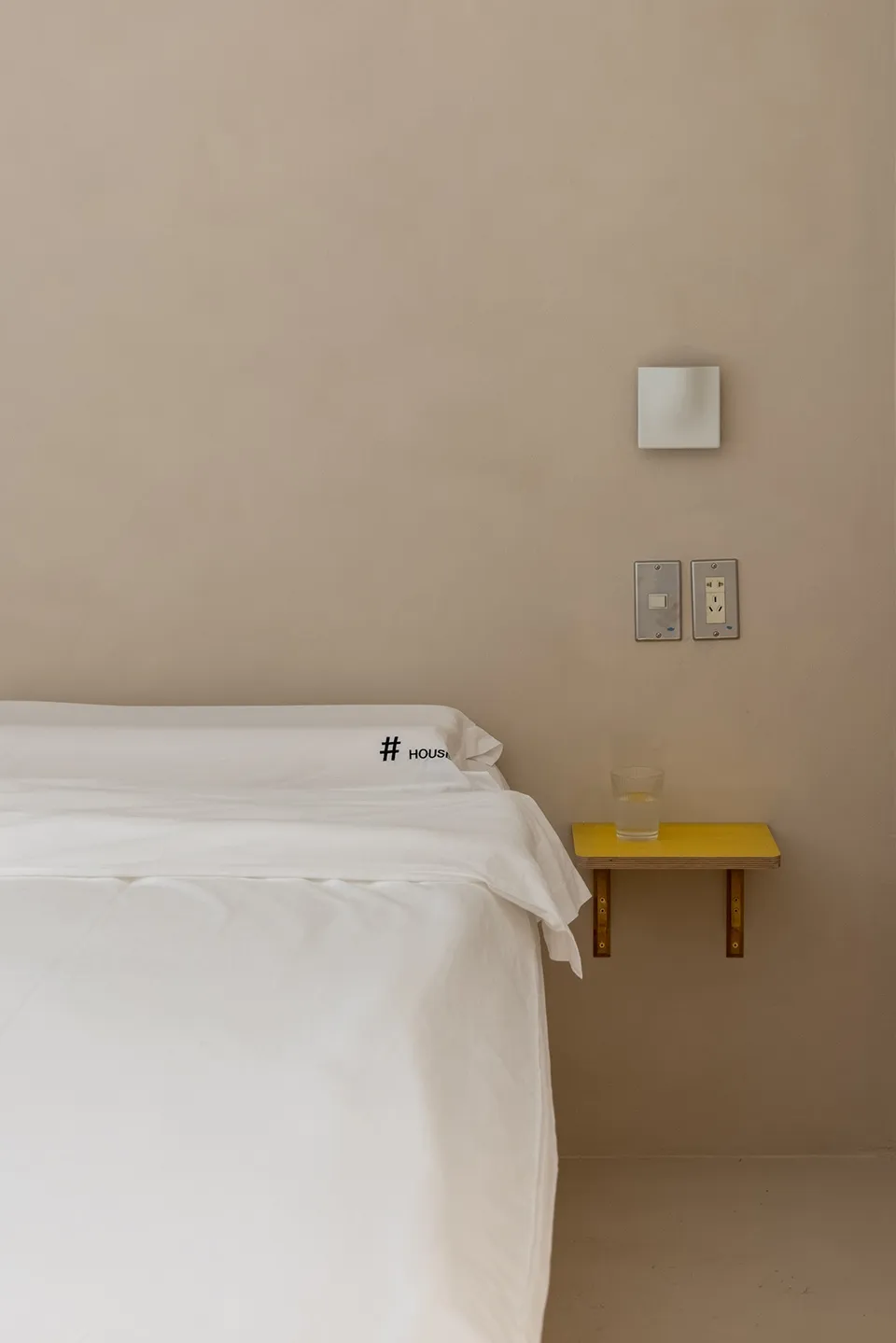 A minimalist bedroom with white textiles on a concrete wall.