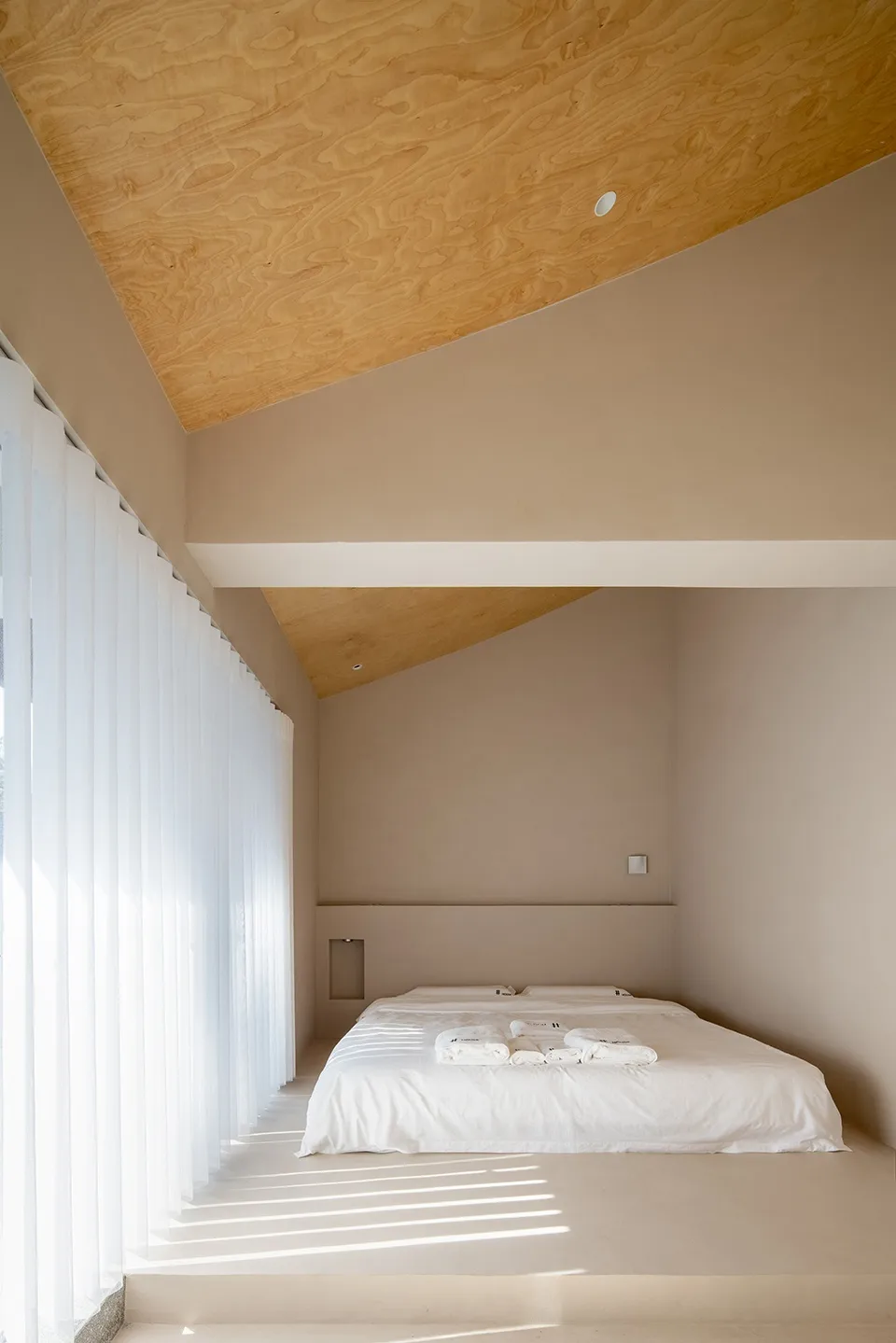 Minimalist bedroom featuring a brown ceiling, concrete floor, and white textiles on the bed.