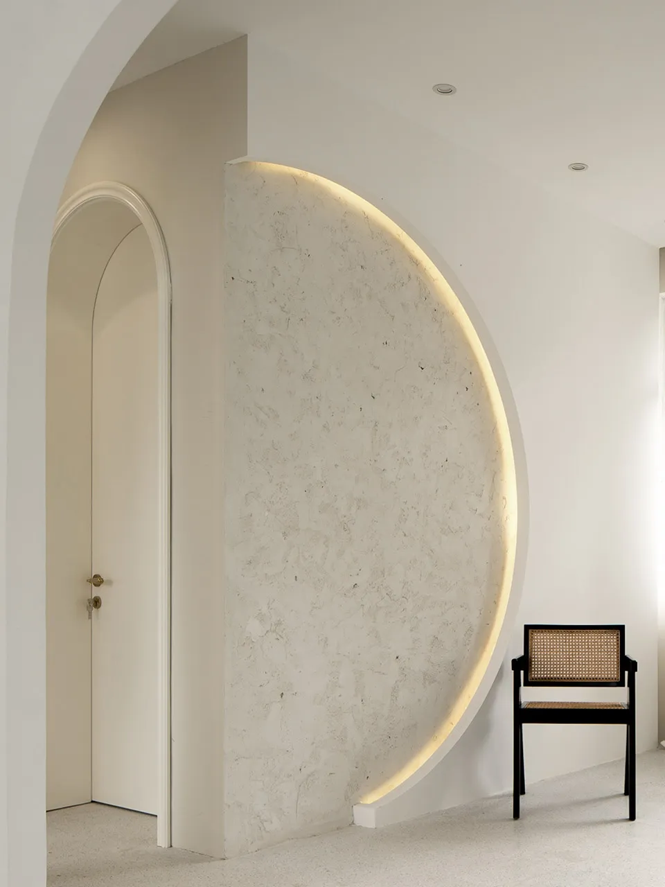 A minimalist interior design featuring a textured cement wall with a circular cut-out and embedded lighting, complemented by