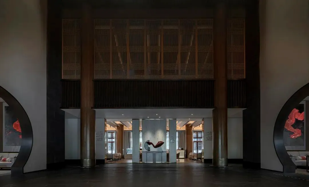Modern hotel lobby featuring concrete columns and floors, with a large sculpture in the center.