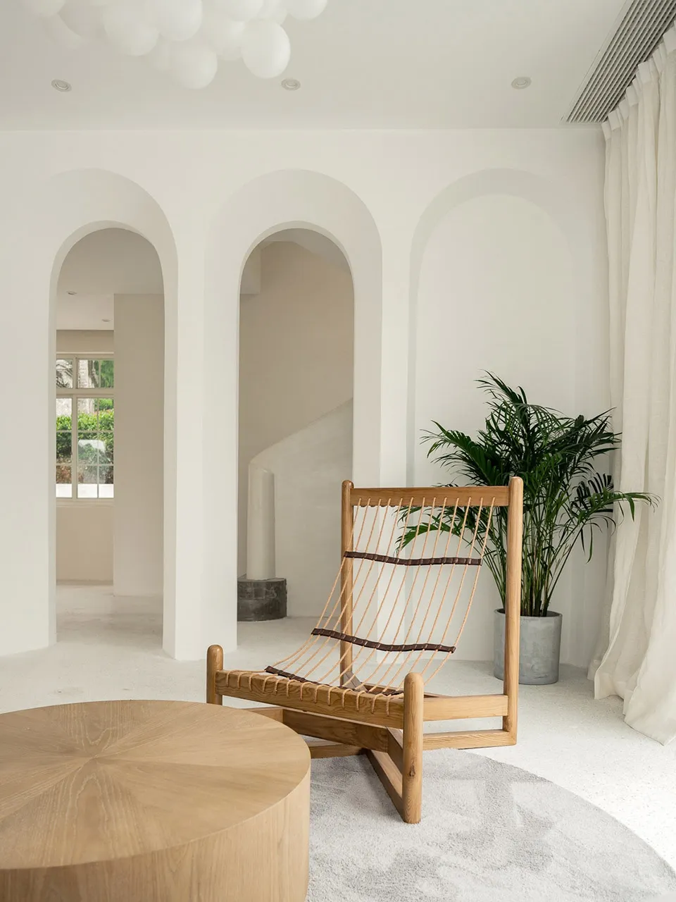 A minimalist living room with a wooden chair, coffee table, and potted plant.