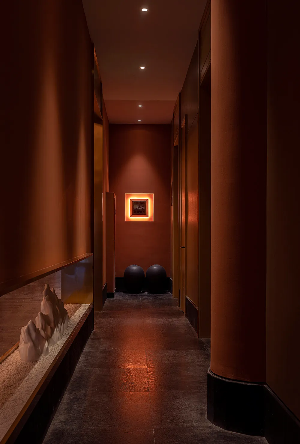 A minimalist corridor with concrete flooring and walls, lit by recessed lighting.