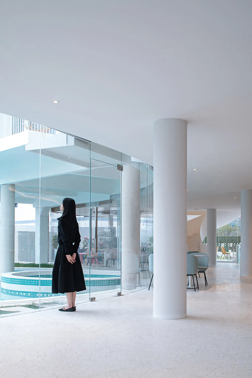 A modern interior design featuring a glass-walled lounge area with a poolside view, using concrete and glass materials.