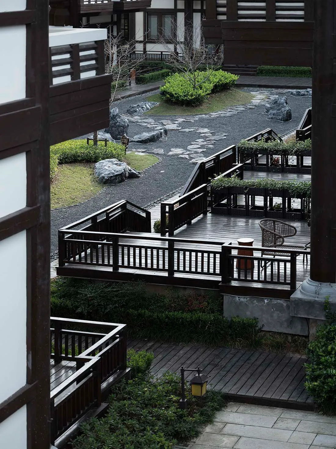 A modern residential garden featuring a wooden pathway surrounded by greenery and rocks.