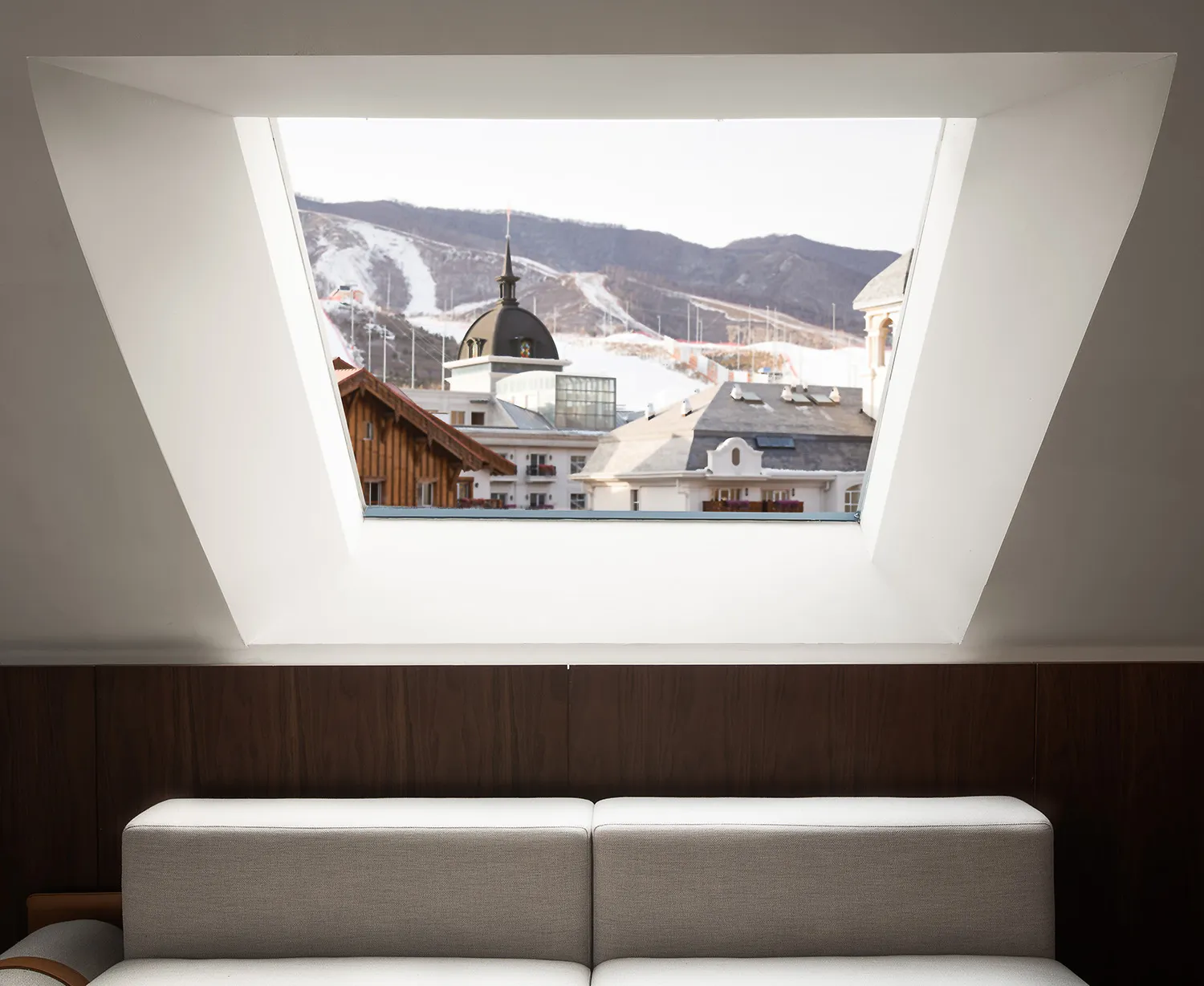 A white sofa with a view of a snowy cityscape through a large window.