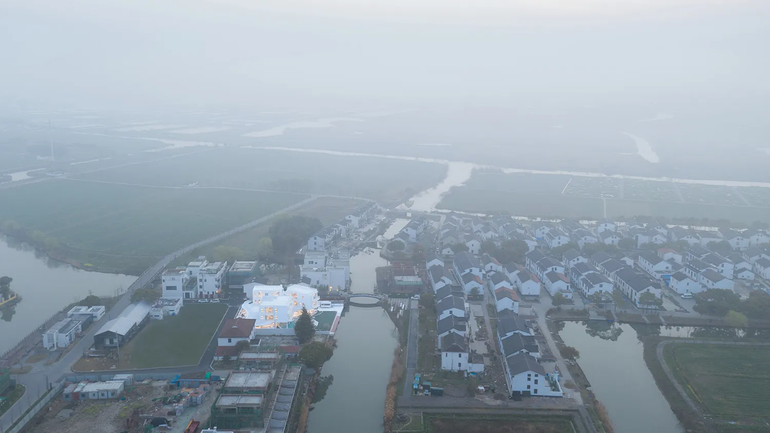 從上方俯瞰,一座有白色建築和小屋的村落,周圍環繞著綠樹與田野。