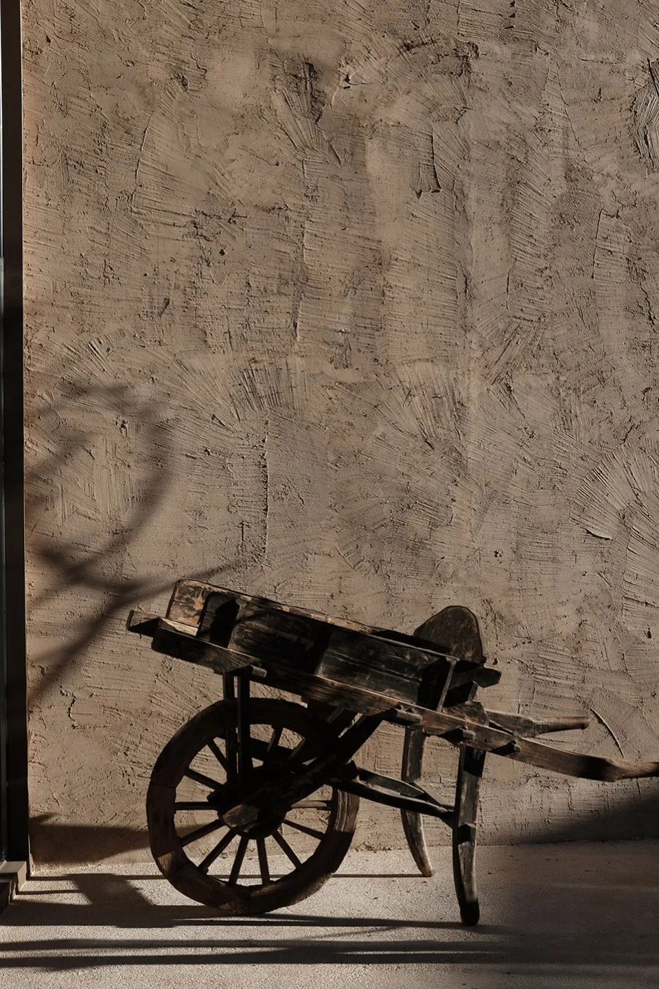 A rustic wooden wheelbarrow leaning against a textured concrete wall.