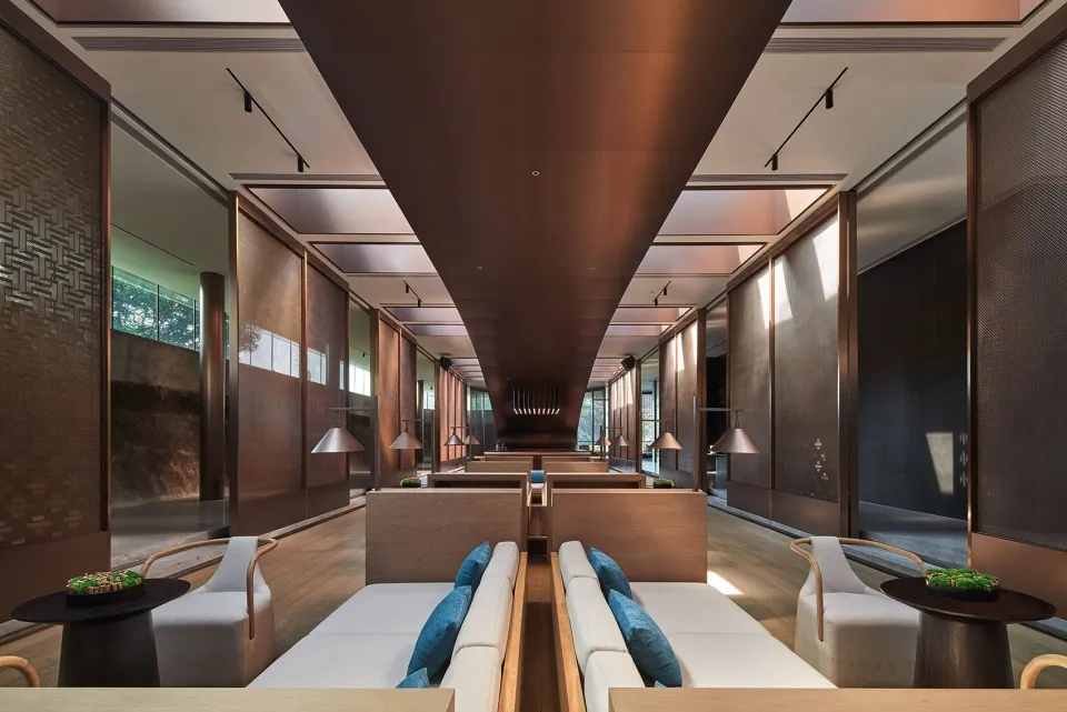 A contemporary hotel lounge area with wooden furniture, concrete flooring, and decorative room dividers.
