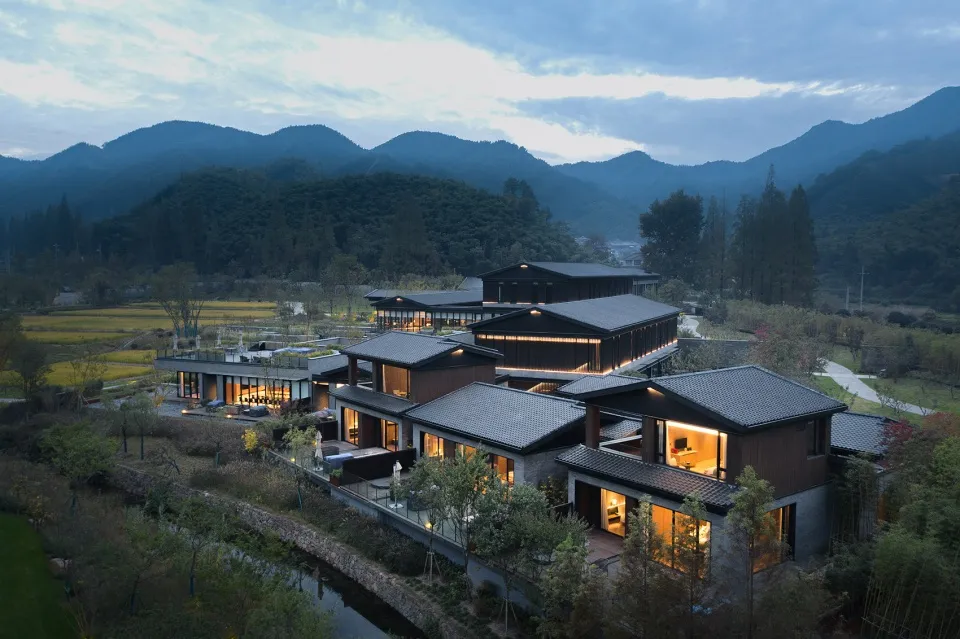 A modern residential retreat featuring brick and concrete structures surrounded by lush greenery and mountains in the backgro