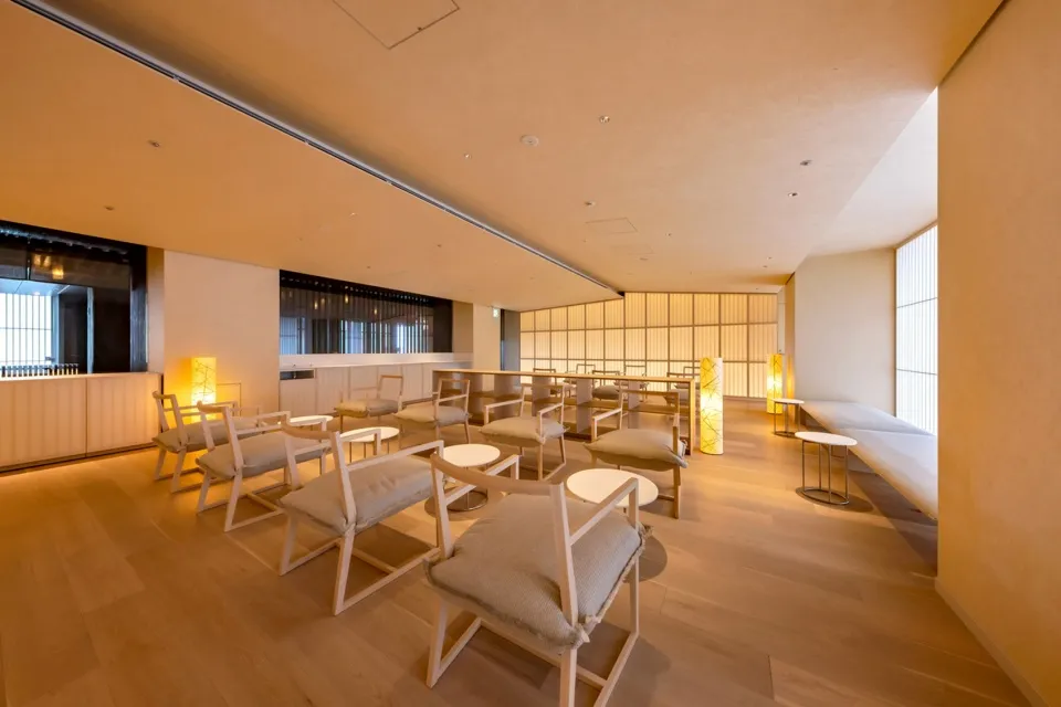 Interior of a modern restaurant with wooden flooring, cushioned chairs, and warm lighting.