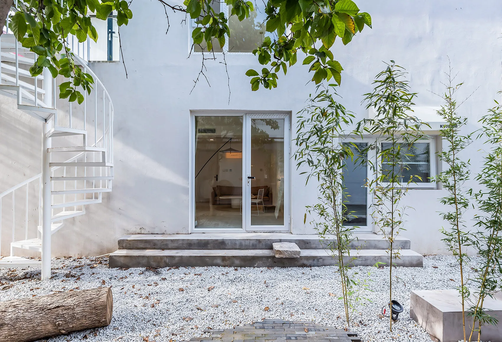 A modern residential exterior with concrete steps, gravel ground cover, and a spiral staircase.