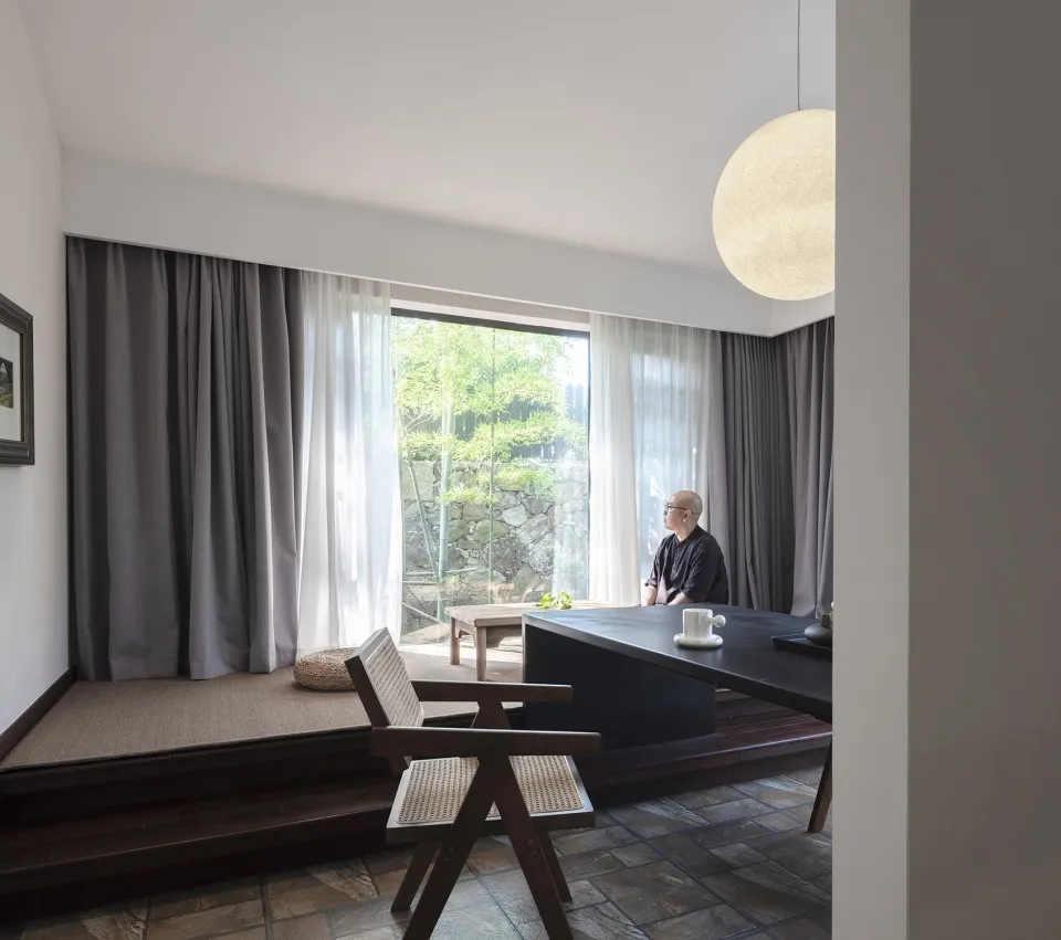A minimalist study space featuring wood disc chairs and a black desk in front of large windows.