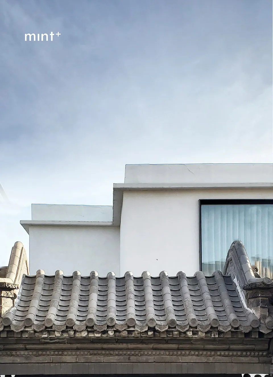 Modern building with white walls and concrete roof tiles against a cloudy sky.