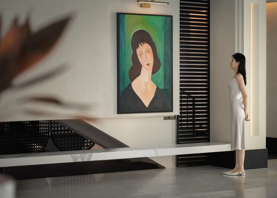 A minimalist modern living room featuring a woman with brown hair dressed in green standing in front of a painting of a woman