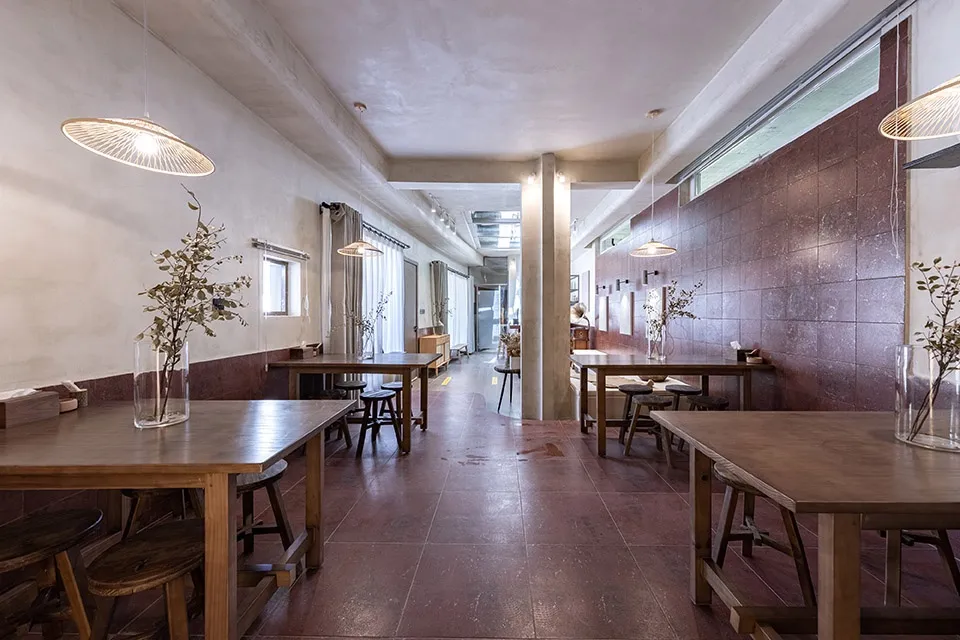 Minimalist cafe interior with exposed concrete walls, wood tables, and terrazzo floor tiles.