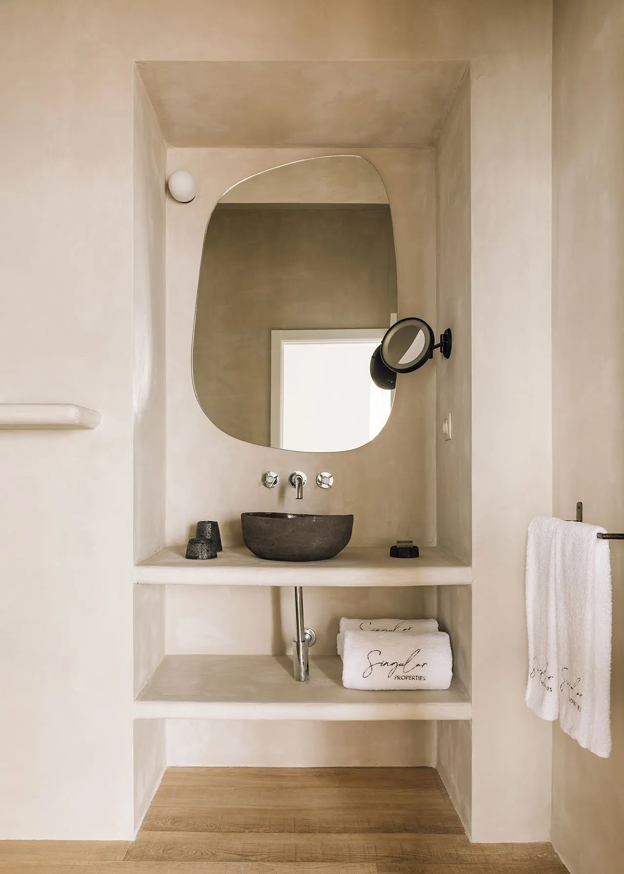 A minimalist bathroom with a concrete sink, wall-mounted faucet, and a round mirror above it. The space is adorned with white