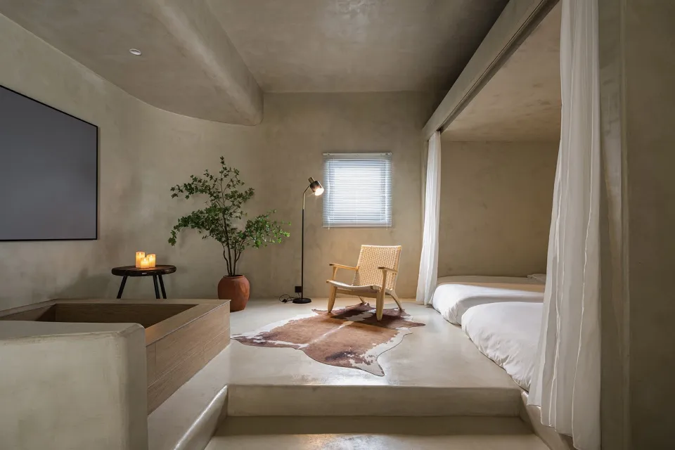 A minimalist bedroom with concrete flooring, a chair, a plant, and a floor lamp.