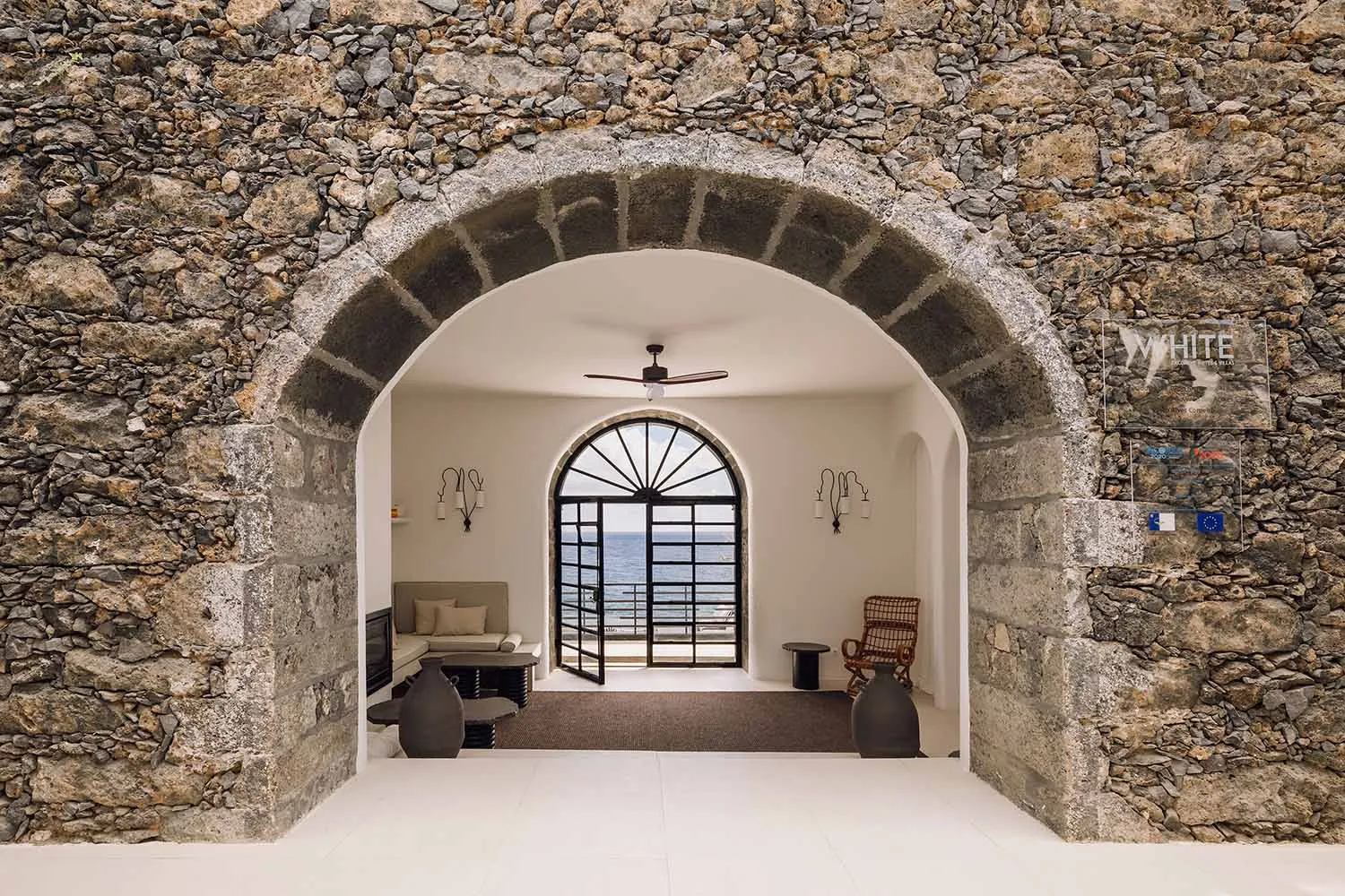 A minimalist interior entryway with stone walls, an arched doorway, and ocean view.