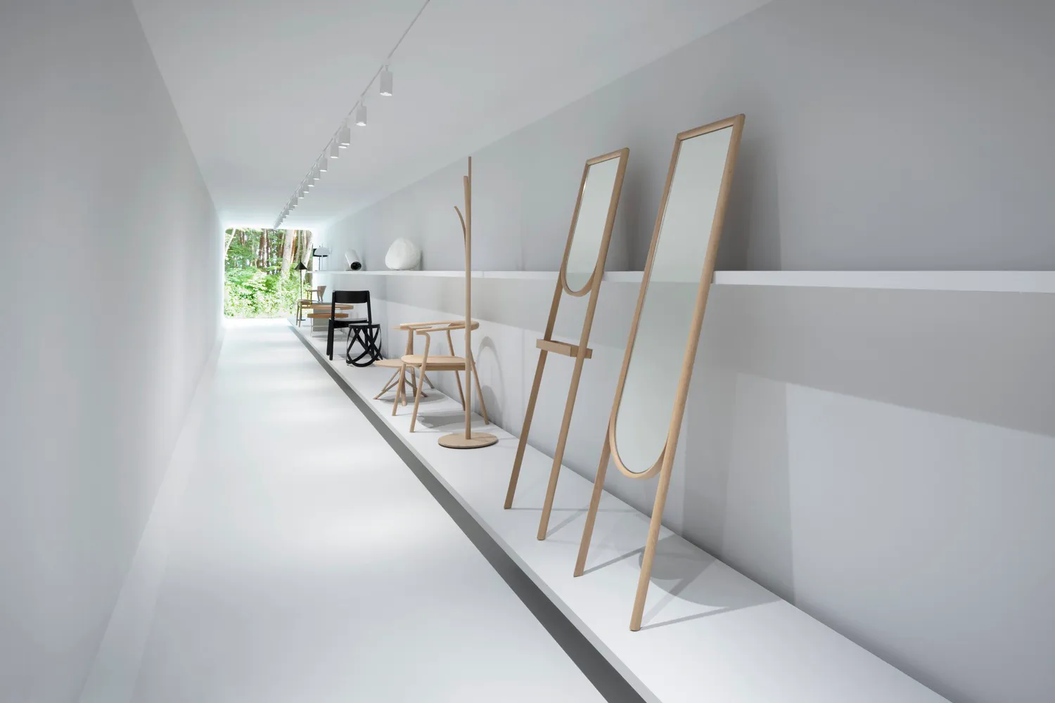 Minimalist furniture display featuring white wooden stands and mirrors in a white corridor.