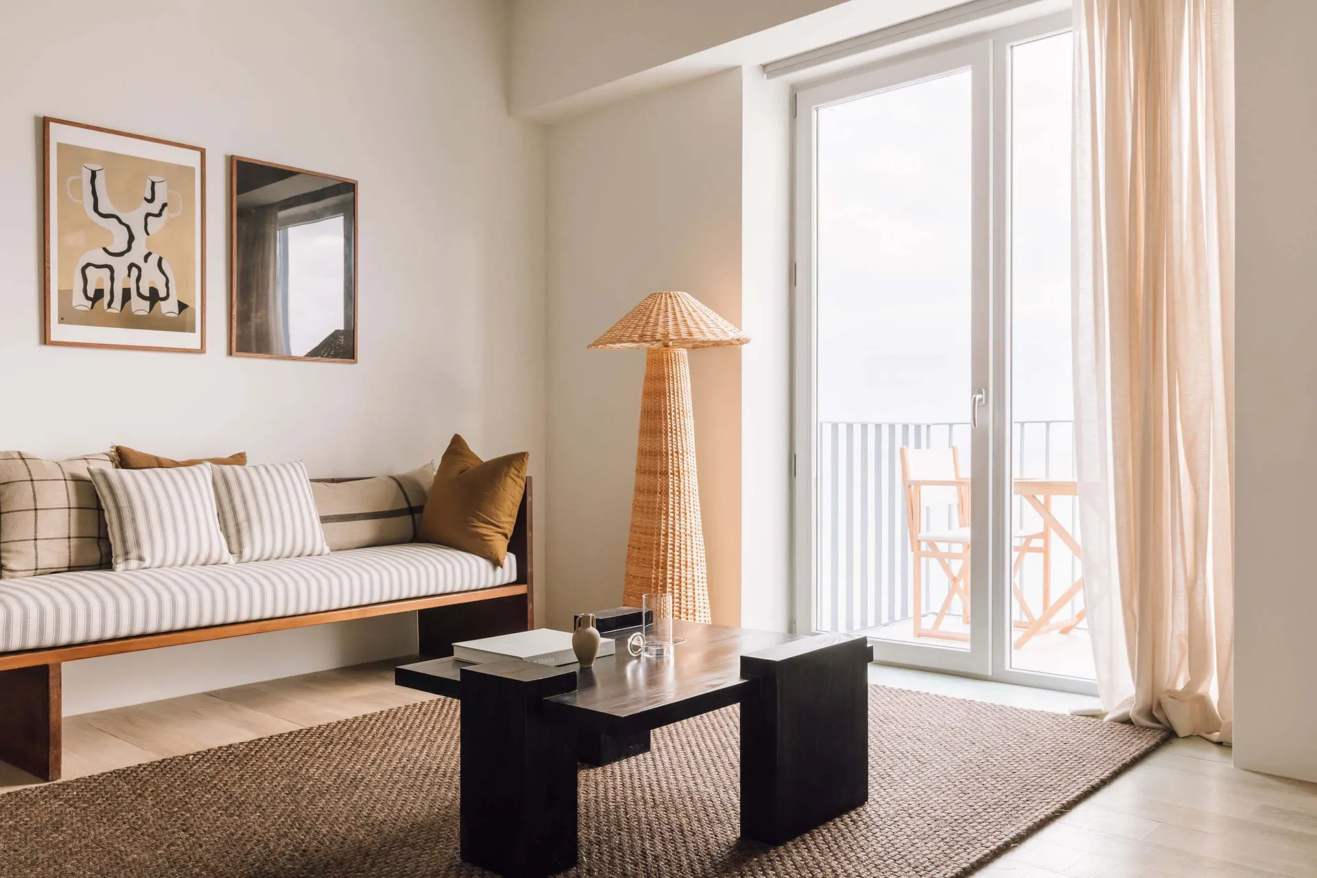 A minimalist living room featuring a daybed, coffee table, and a woven lamp.