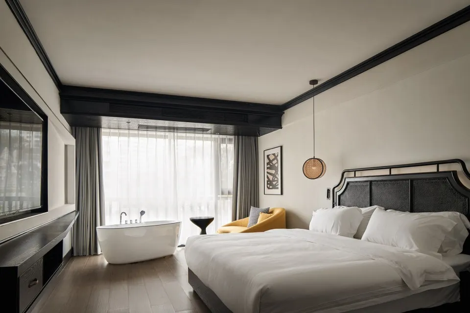 Modern minimalist bedroom with a white bed, yellow armchair, and white bathtub under a large window.