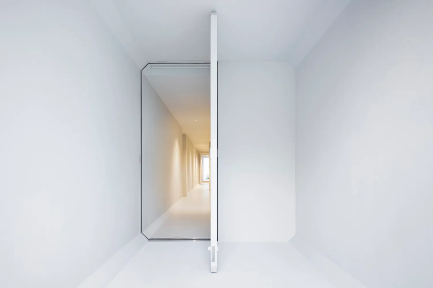 A minimalist white interior space with a glass door leading to a corridor.