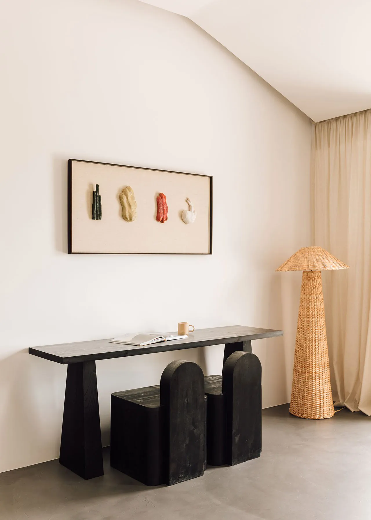 A minimalist living space featuring a sleek black console table, a wicker floor lamp, and a contemporary wall installation.