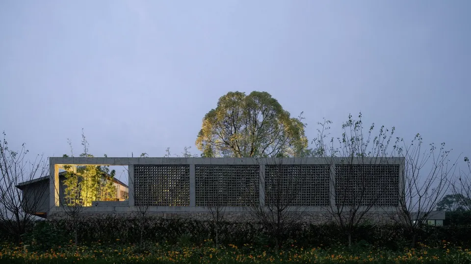 A modern concrete structure with a lattice facade, surrounded by trees and flowers.