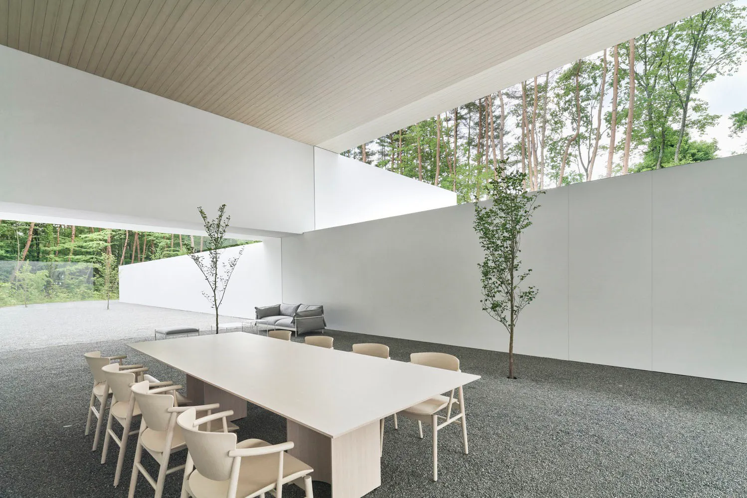 Modern, minimalist conference room with white walls and concrete floor, featuring a long white table and chairs.